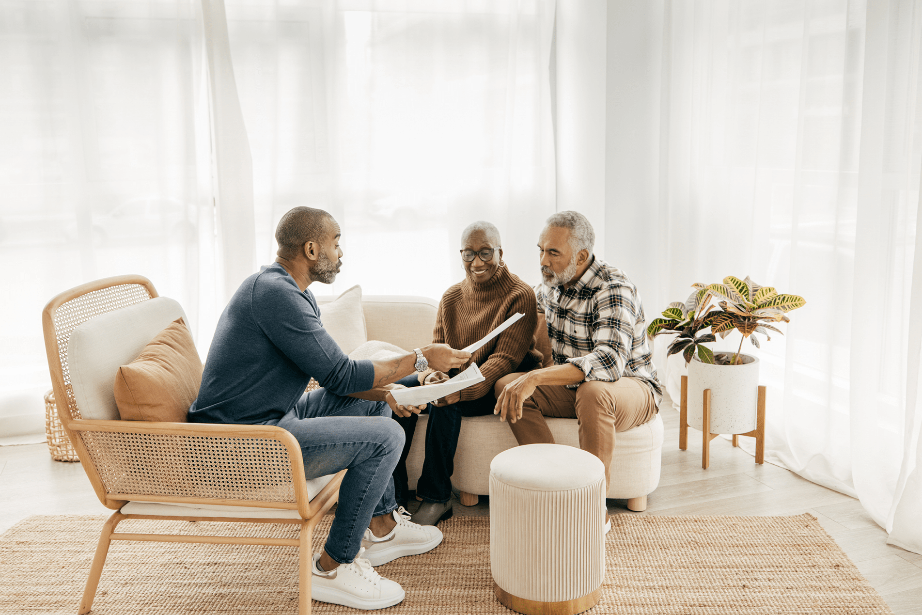 Three care navigators engaged in a discussion while seated in a well-lit living room setting, with one person presenting a document to the other two.