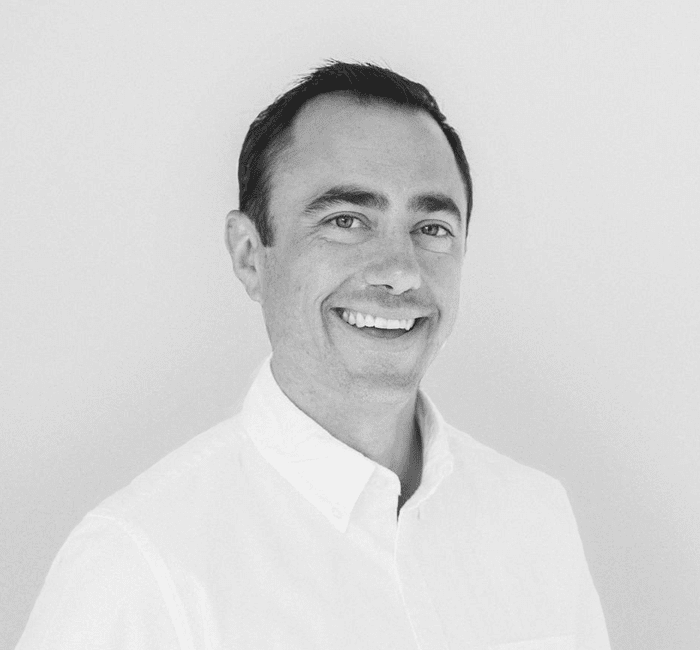 A smiling man wearing a white shirt against a plain background.