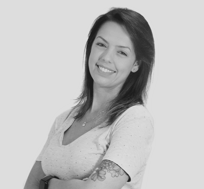 A smiling woman in a casual shirt with a tattoo on her arm, depicted in a black and white photo.