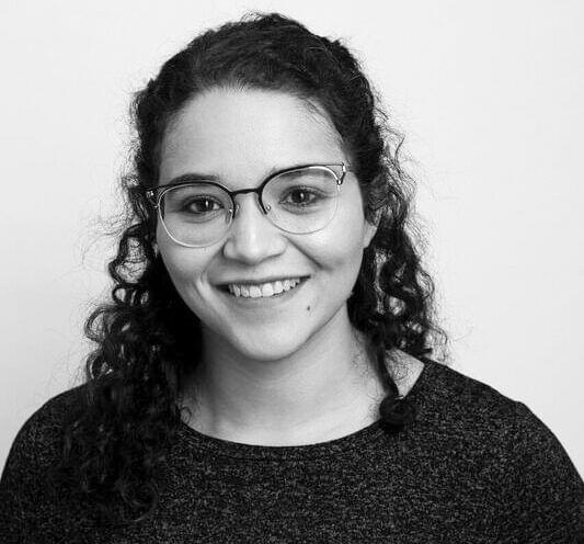 A smiling woman with curly hair and glasses against a plain background.