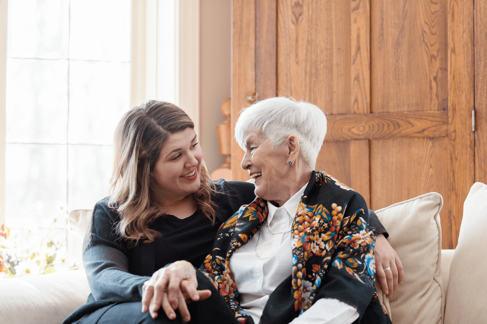 Two women of different generations sharing a joyful moment together on a couch, illustrating the essence captured in Trualta's press releases.