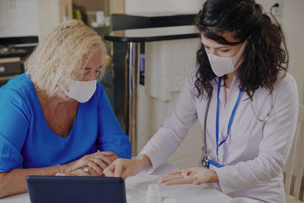 Healthcare professional in a mask discussing information related to Covid-19 with an elderly patient, who is also wearing a mask.