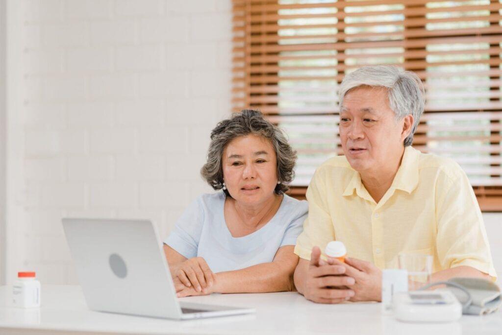 Senior couple and their caregivers reviewing medication information on a laptop at home.