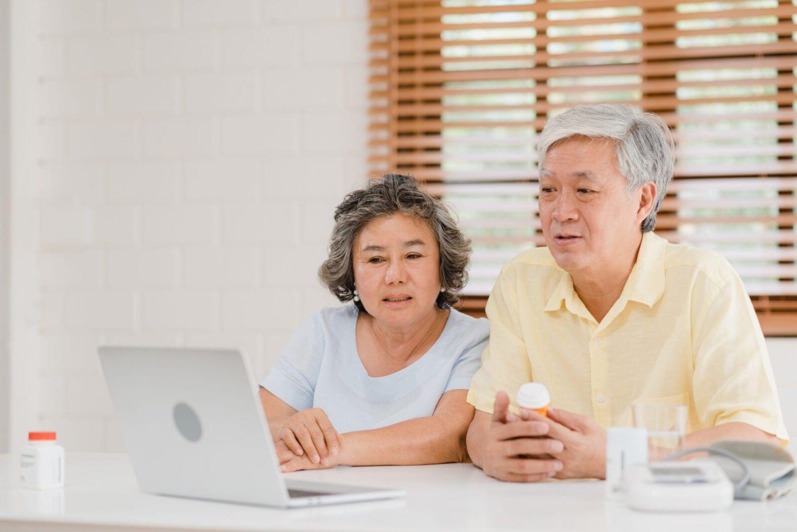 Senior couple and their caregivers reviewing medication information on a laptop at home.