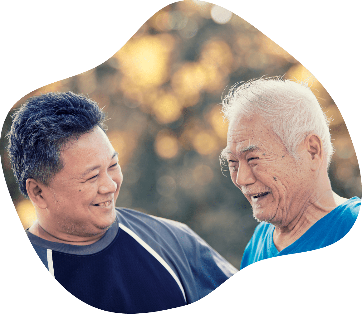 Two men smiling at each other, one older and one middle-aged, with a blurry natural background.