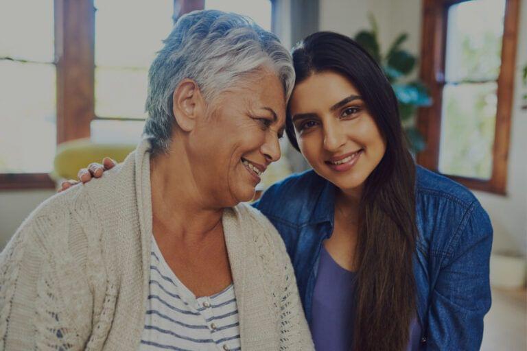 A smiling young woman, demonstrating soft skills, embracing an older woman who is also smiling.