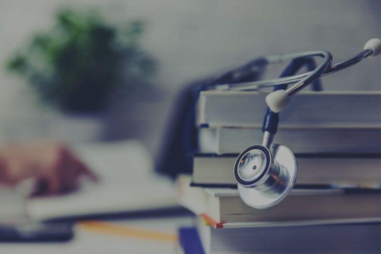 Stethoscope on a stack of books with accessible information for mitigating low caregiver health literacy, and a person studying in the background.