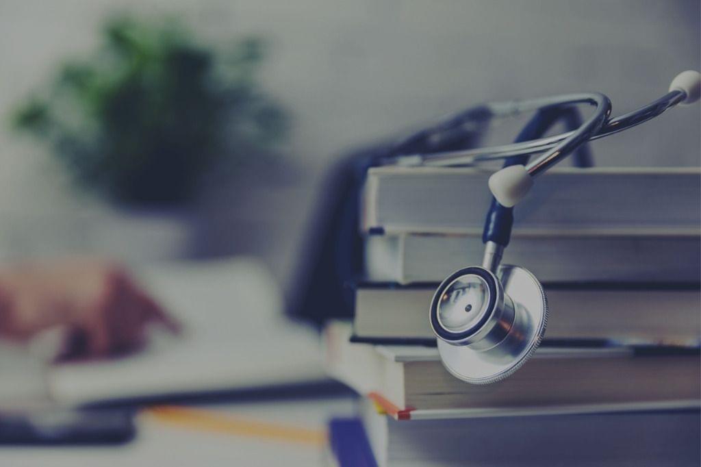Stethoscope on a stack of books with accessible information for mitigating low caregiver health literacy, and a person studying in the background.
