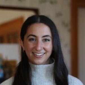 A smiling woman with dark hair wearing a white turtleneck sweater is exploring new employment opportunities.
