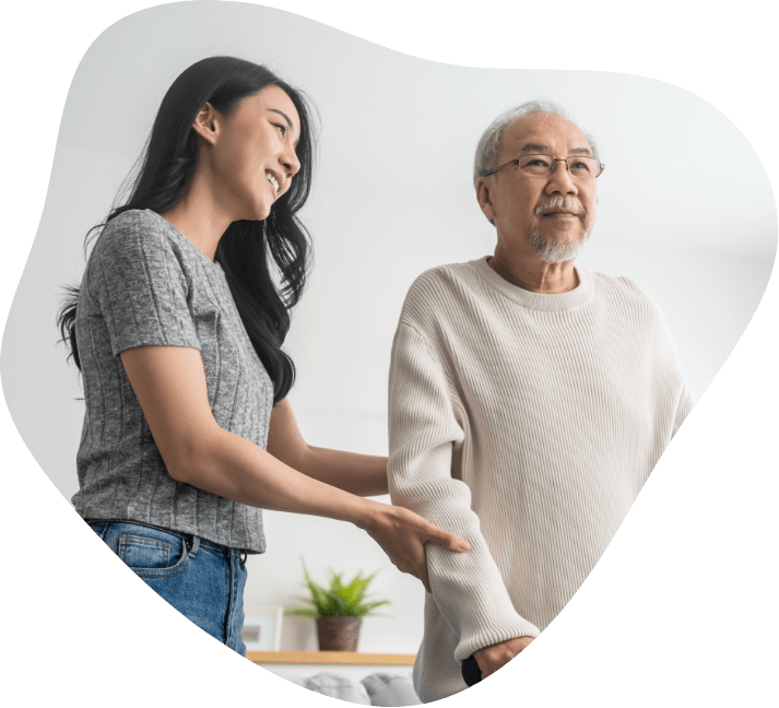 A young woman holding hands with an elderly man in a comforting gesture, both standing indoors.
