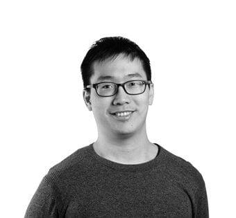 Young man with glasses smiling at the camera against a white background.