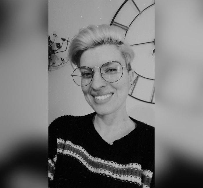 Person with short hair and glasses smiling at the camera in a black and white photo.