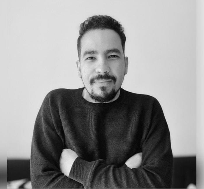 A black and white portrait of a smiling man with crossed arms, wearing a black sweater.