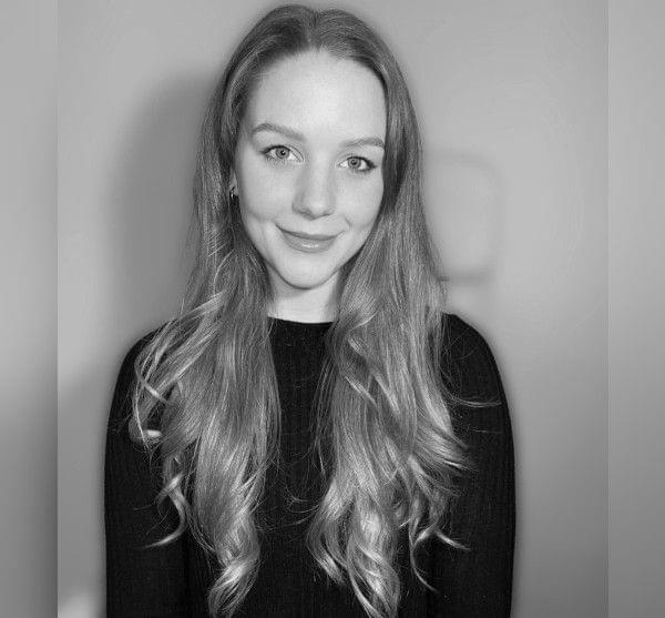 A black and white portrait of a smiling woman with long, wavy hair.