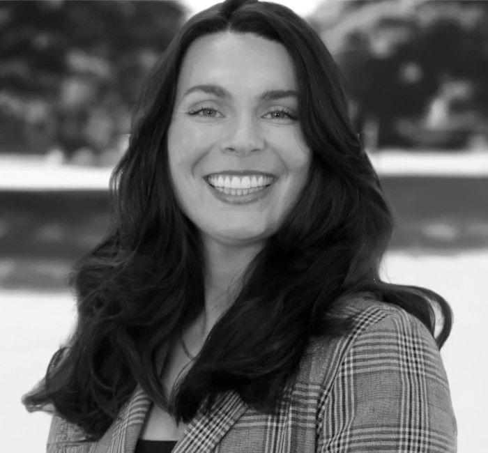 Black and white portrait of a smiling woman with long hair, wearing a plaid jacket.