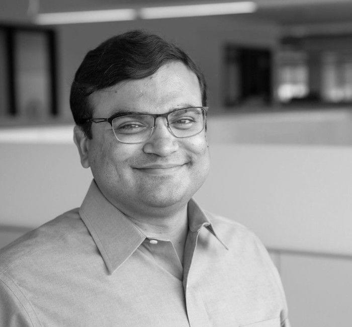 A black and white portrait of a smiling man wearing glasses and a button-up shirt.