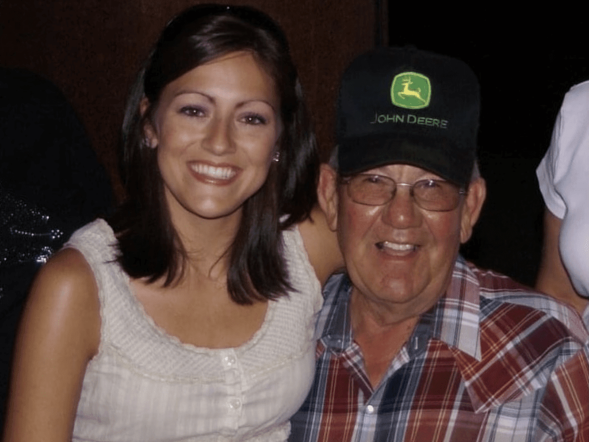A smiling woman and a man wearing a john deere cap pose for a photo together.
