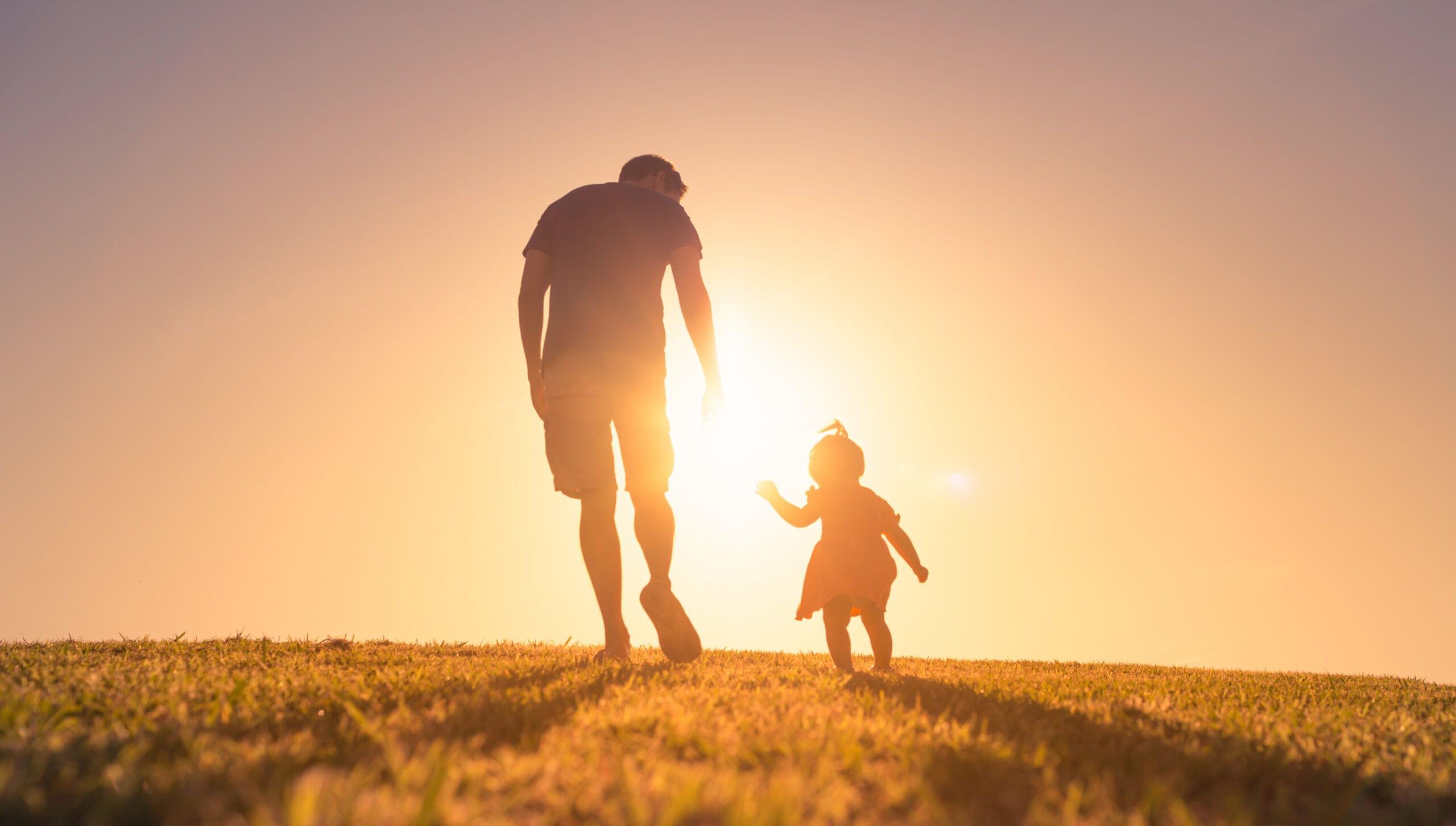 Father and his little daughter walking in the park at sunset.